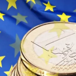 Stos monet euro na tle flagi Unii Europejskiej, oświetlenie studyjne podkreśla detale monet.