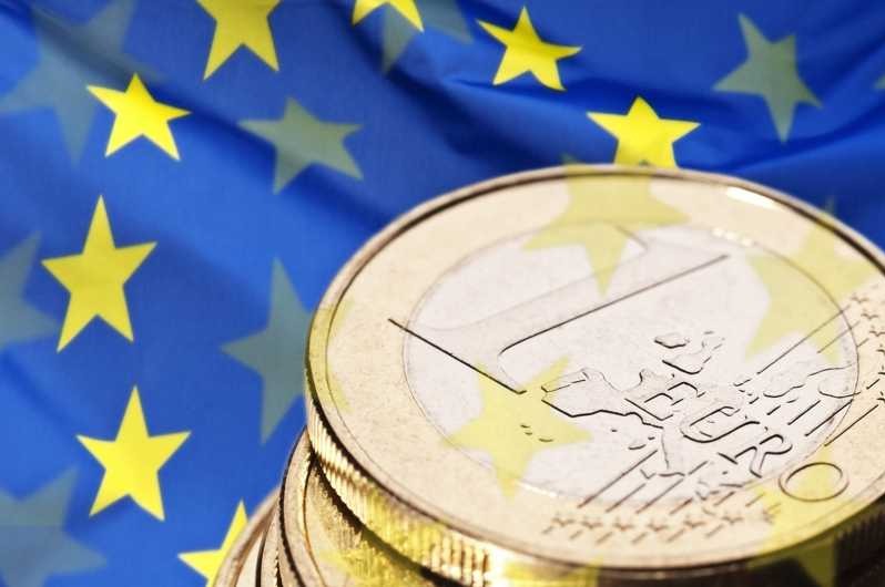 Stos monet euro na tle flagi Unii Europejskiej, oświetlenie studyjne podkreśla detale monet.