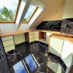 Nowoczesne wnętrze poddasza z czarną marmurową podłogą odbijającą światło z okien dachowych, zabudowa meblowa w jasnych odcieniach z drewnianymi blatami, ściana wykończona płytami z czarnego marmuru.