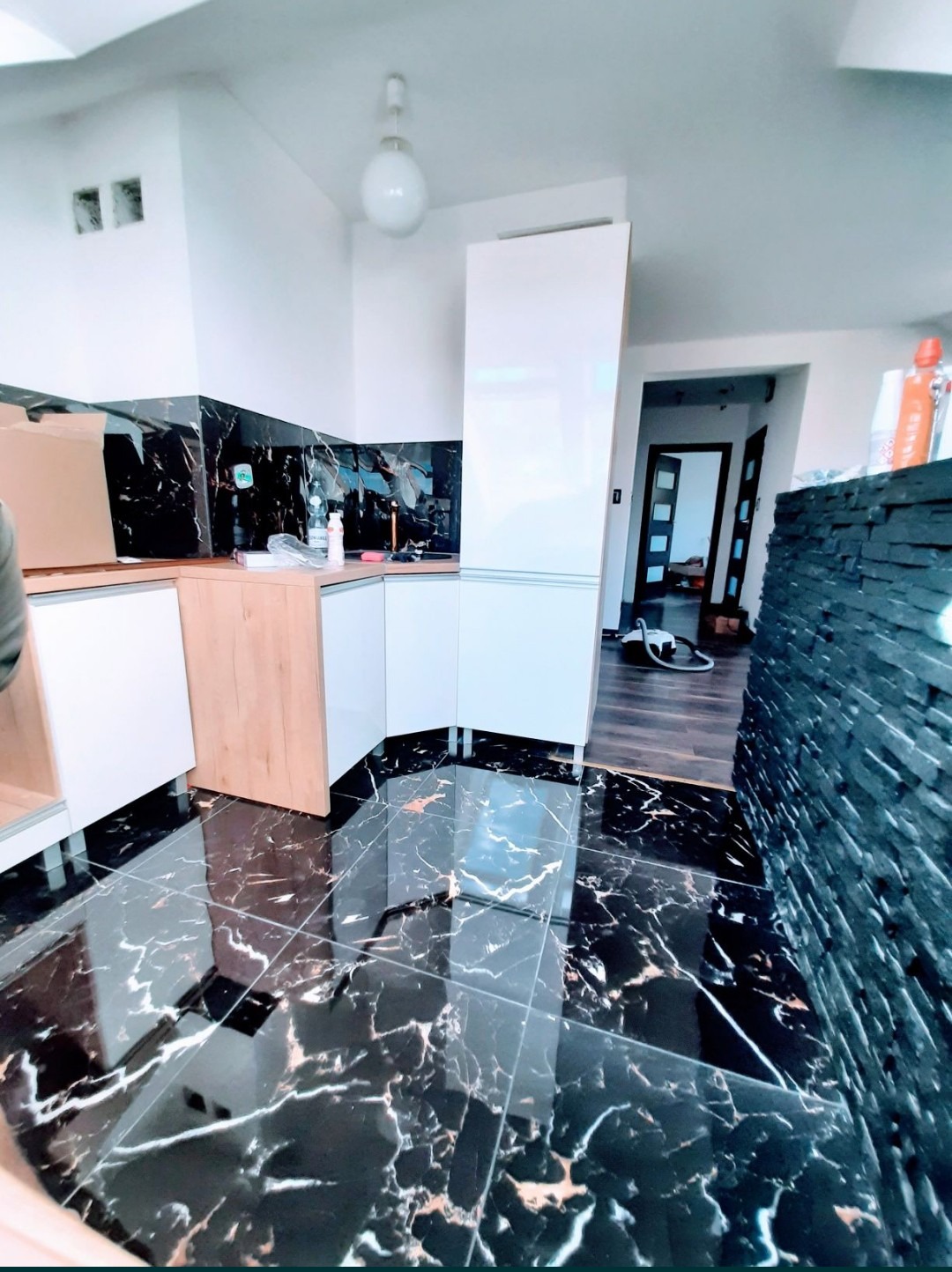 Częściowo zamontowana zabudowa kuchenna z czarnym marmurowym blatem i pasującą podłogą w mieszkaniu w Chełmnie, widoczny fragment ściany z kamienia dekoracyjnego.