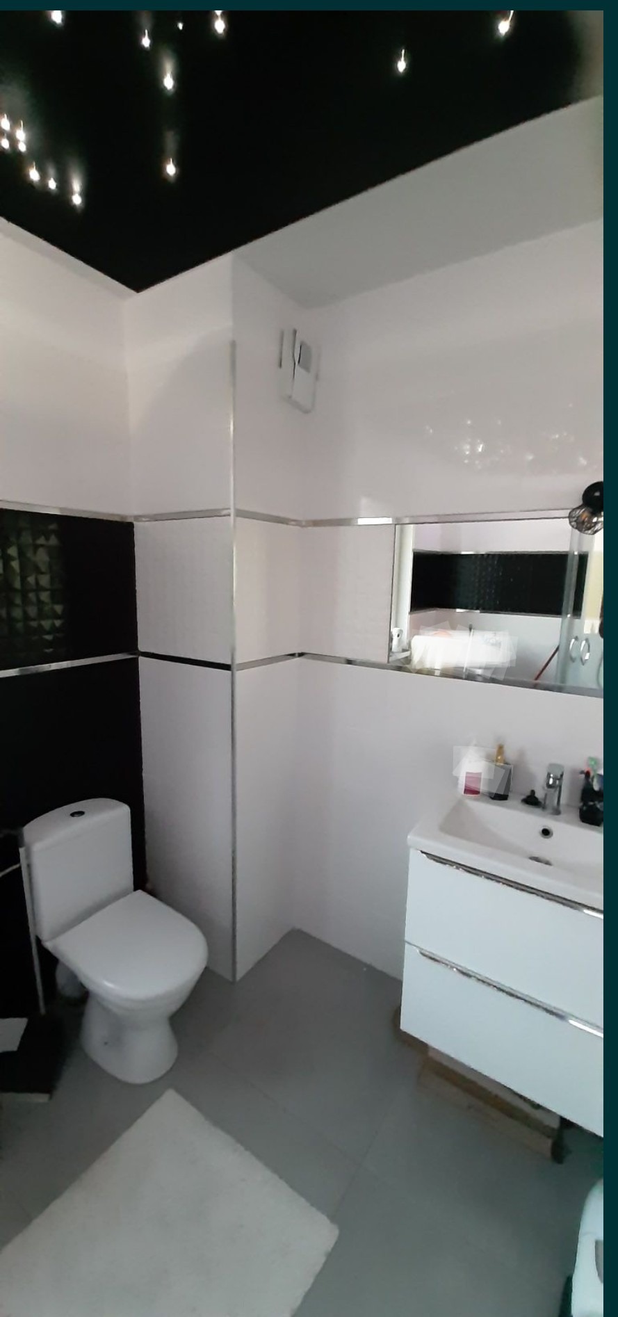 Nowoczesna łazienka w czarno-białej kolorystyce z podwieszanym sufitem z punktowym oświetleniem, białą ceramiką i szarą podłogą.