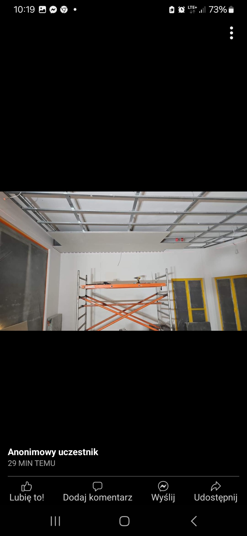 Montaż sufitu podwieszanego z płyt kartonowo-gipsowych na metalowej konstrukcji, widoczne rusztowanie i zabezpieczone folią okna.