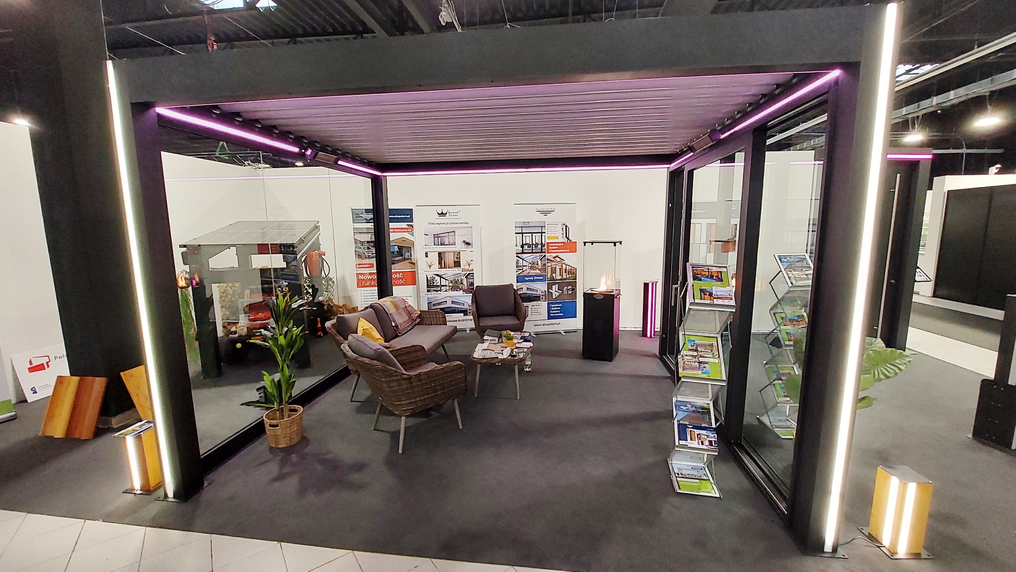 Nowoczesna pergola z oświetleniem LED RGB w słupach i belkach, tworząca wyjątkowy klimat. Wnętrze z meblami i dekoracjami, materiały reklamowe w stojakach.