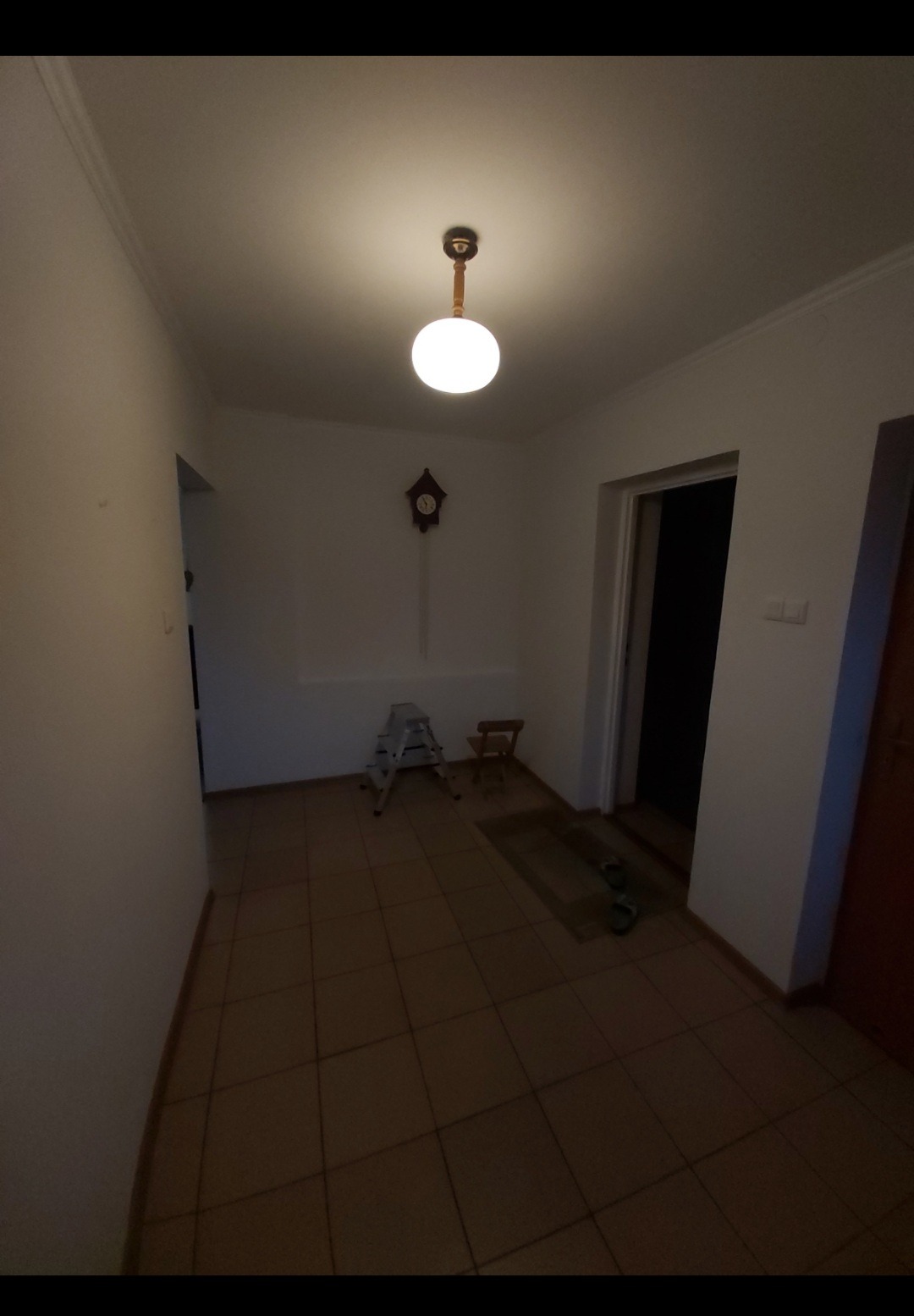 Korytarz z terakotową podłogą, drabinką malarską, zegarem z kukułką i lampą sufitową w stylu retro.