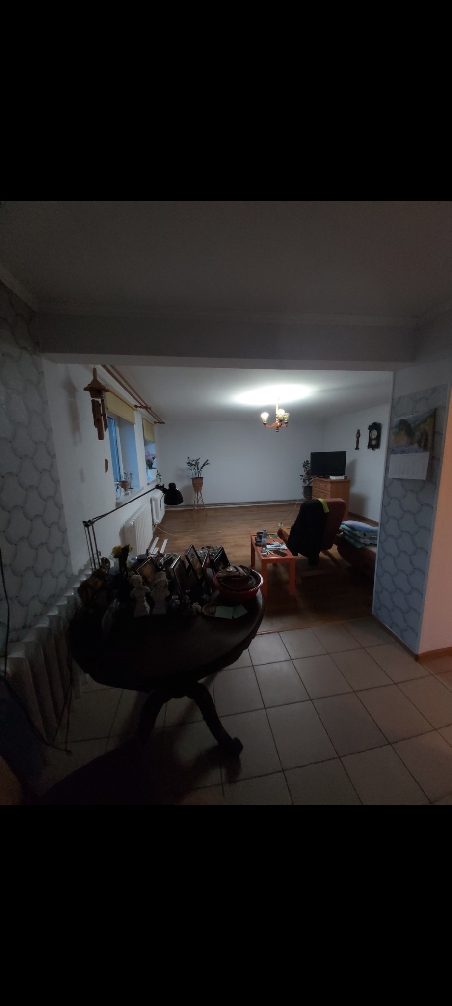 Widok na salon połączony z pokojem, z widoczną ścianą z dekoracyjną tapetą i klasyczną aranżacją wnętrza, w tym drewnianą podłogą i meblami.