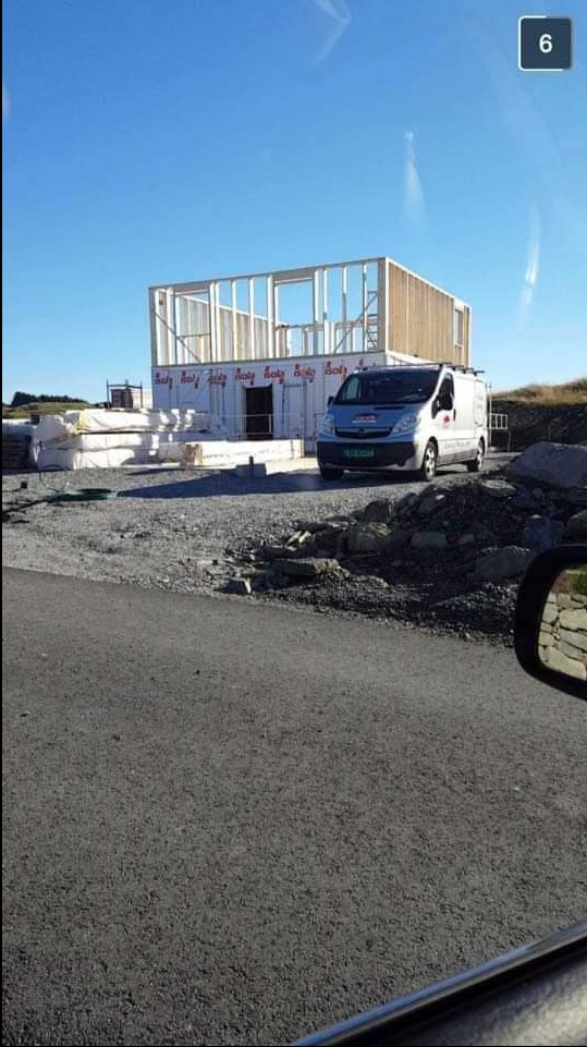 Wznoszony dom szkieletowy z drewnianą konstrukcją, obok zaparkowany van. Widok z perspektywy kierowcy.