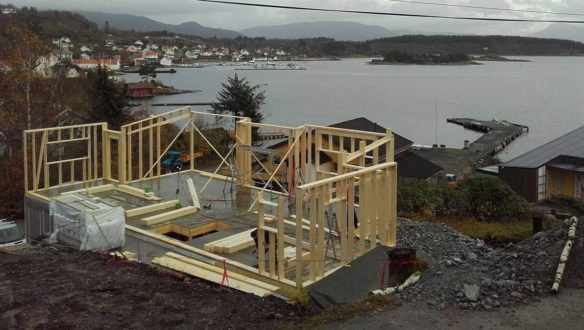 Konstrukcja szkieletowa domu w trakcie budowy z widokiem na jezioro i górzysty krajobraz w tle, z elementami krajobrazu miejskiego w oddali.