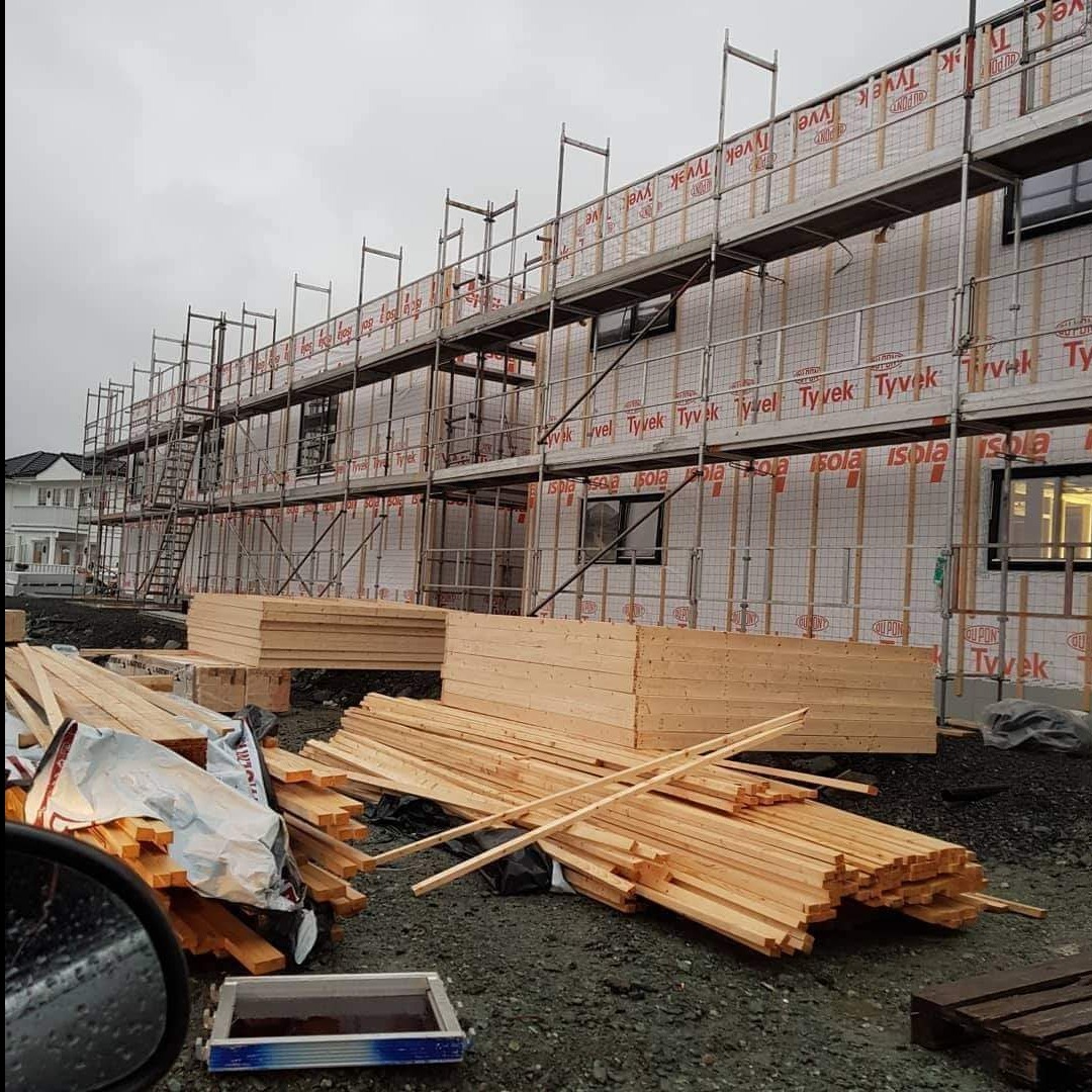 Budowa domu szkieletowego w trakcie: drewniane elementy konstrukcyjne na placu budowy, rusztowania przy ścianach pokrytych membraną izolacyjną. Widok z zewnątrz.