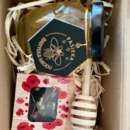 Kosz prezentowy: słoik miodu z czarną etykietą 'Pasieka Baryczka Miodu', nabierak i pudełko herbaty w kartonowym pudełku z wypełnieniem.