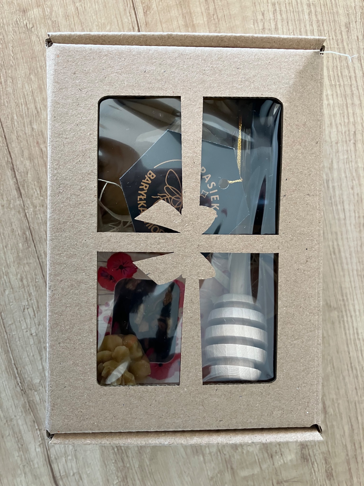 Kartonowy kosz prezentowy z okienkami: miód, czekolada, orzechy i drewniany nabierak do miodu. Widok z góry na drewnianym tle.