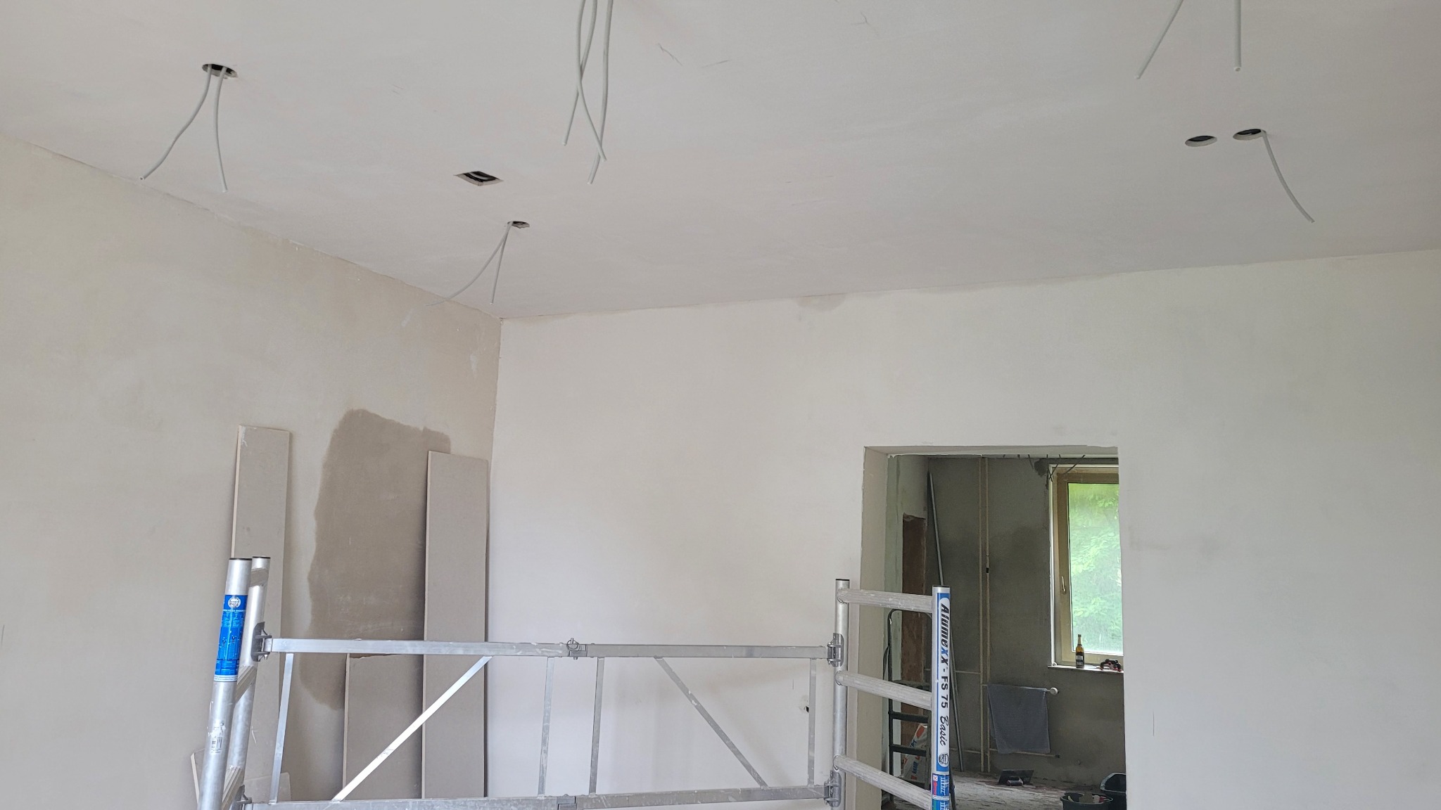 Wnętrze w trakcie prac wykończeniowych w Witten: ściany po szpachlowaniu, widoczne kable wystające z sufitu, częściowo rozłożony aluminiowy ruszt.