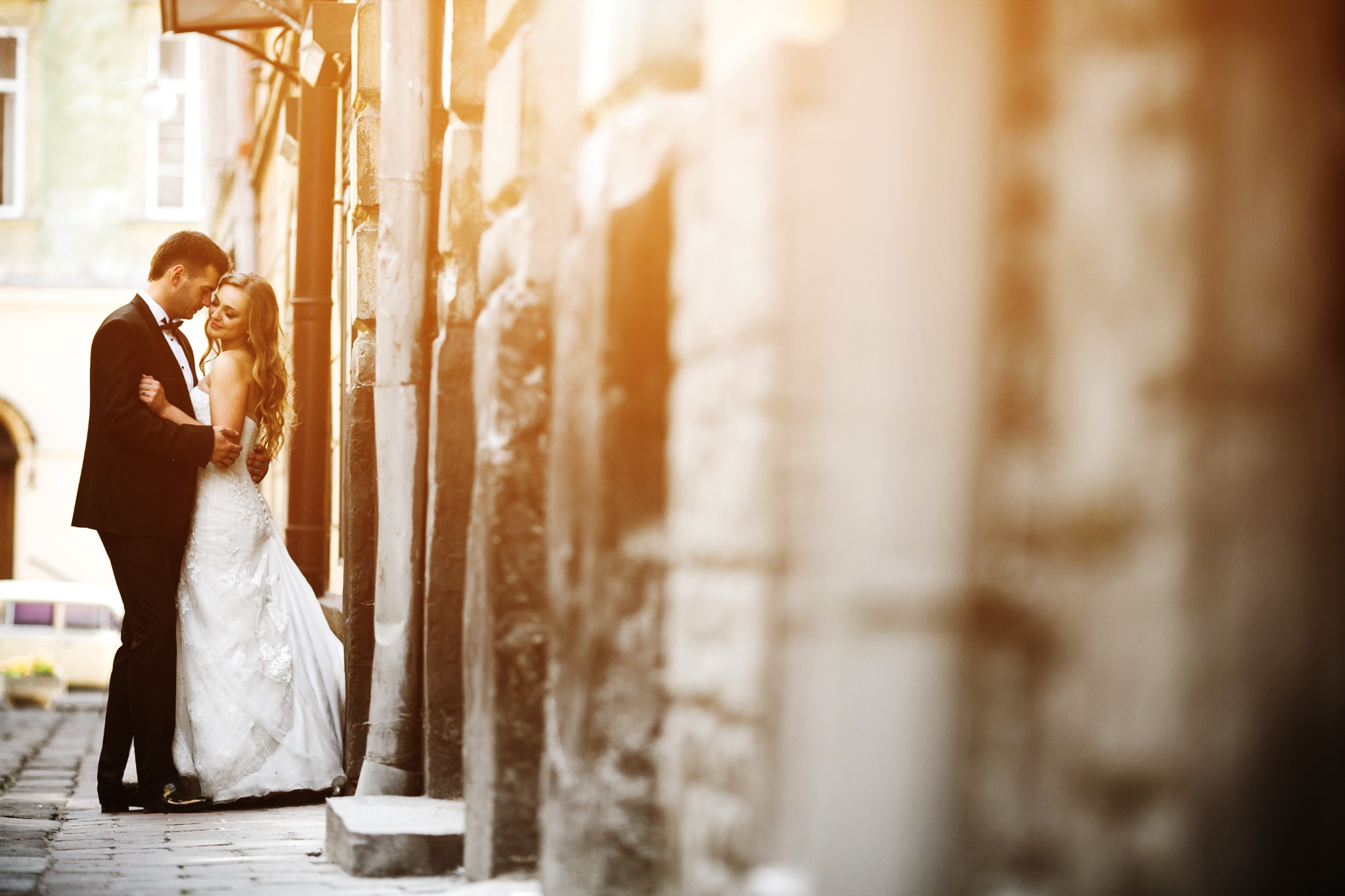 Para młoda w objęciach na tle starej kamienicy z kolumnami, ciepłe światło podkreśla fakturę muru.