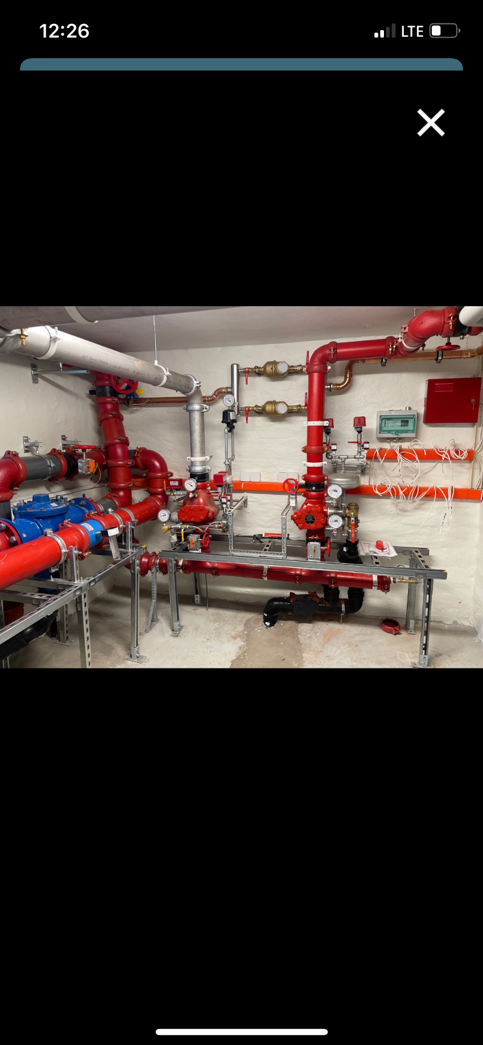 Złożona instalacja rur i zaworów w kolorze czerwonym i niebieskim, zamontowana na metalowych wspornikach w pomieszczeniu technicznym.