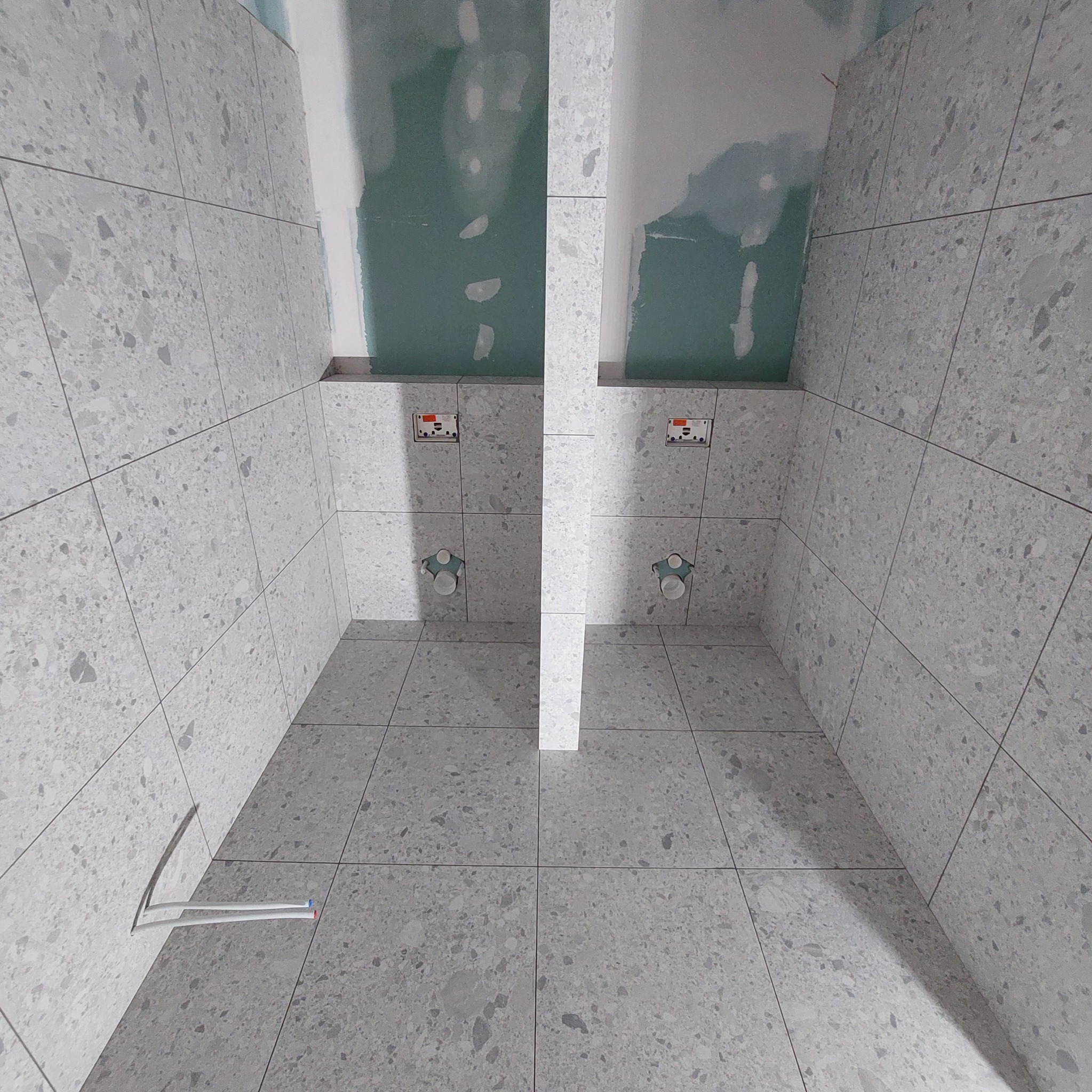 Wnętrze łazienki w trakcie remontu w Jarosławiu: widoczne szare, wzorzyste płytki na ścianach i podłodze, fragmenty niezabudowanej ściany z płyt kartonowo-gipsowych oraz wystające rury.