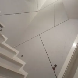 Ściana z płyt kartonowo-gipsowych na poddaszu ze schodami, widoczne otwory na instalacje elektryczne i wykończenie spoin.