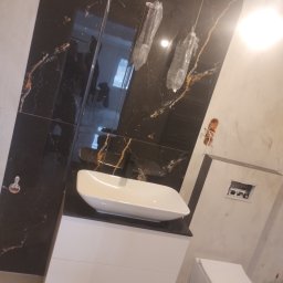 Inwest Dom - Nowoczesna łazienka z czarnymi płytkami imitującymi marmur, białą umywalką nablatową i podwieszaną toaletą. Widoczne elementy instalacji elektrycznej.