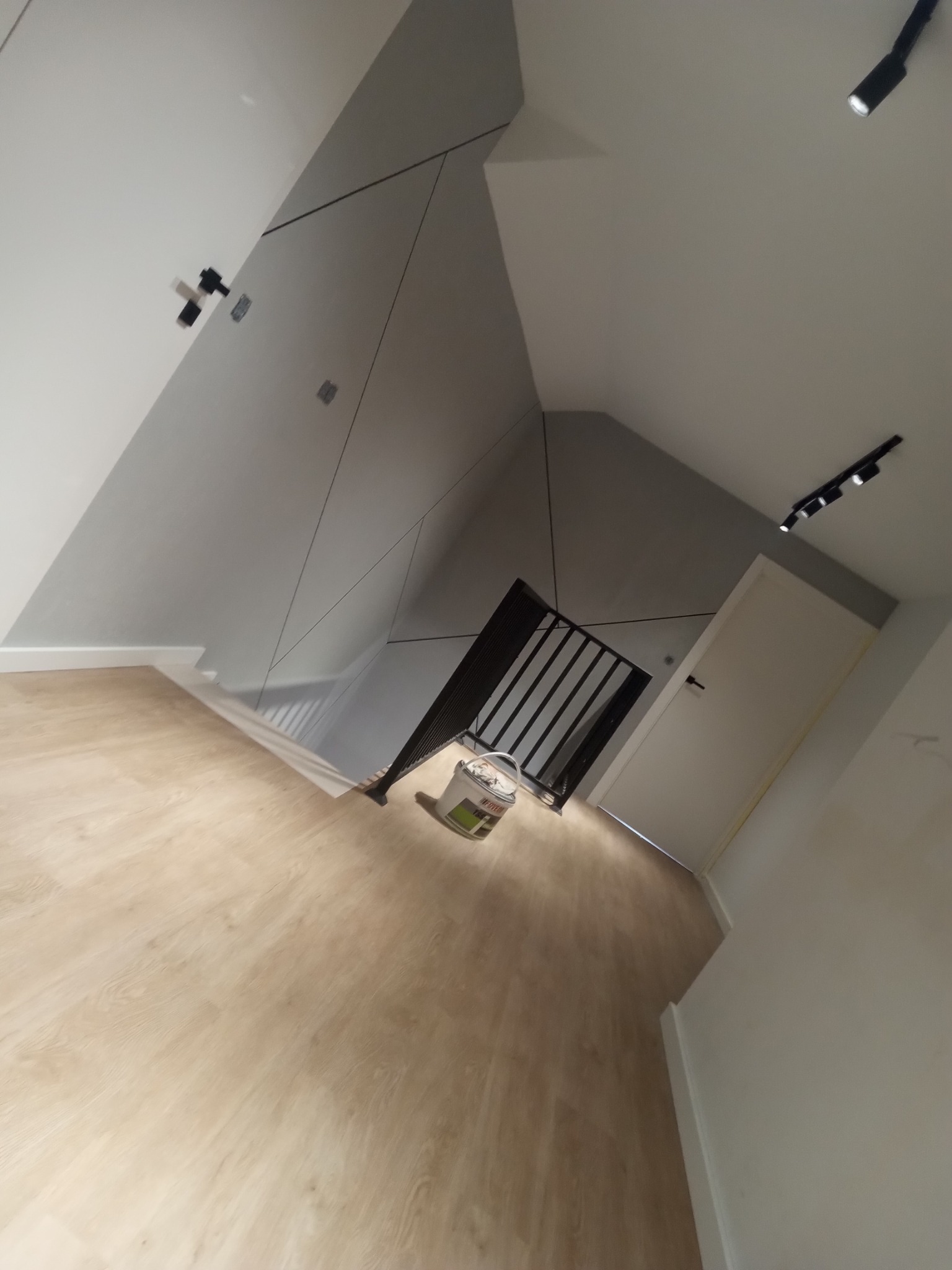 Świeżo wykończone wnętrze z panelami podłogowymi, szarą ścianą z geometrycznymi podziałami, czarną balustradą schodów i białymi drzwiami, widok z góry.