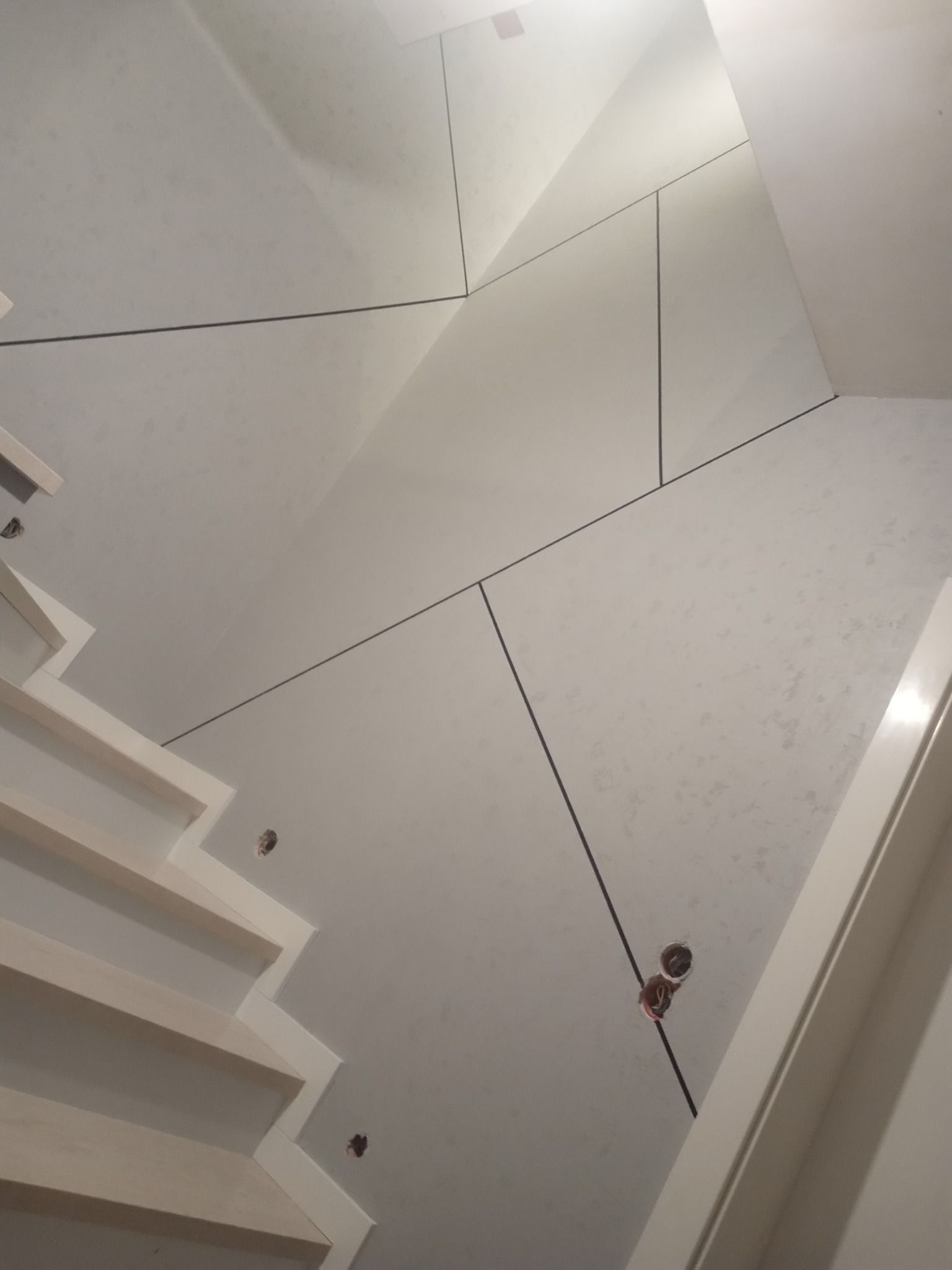 Ściana z płyt kartonowo-gipsowych na poddaszu ze schodami, widoczne otwory na instalacje elektryczne i wykończenie spoin.