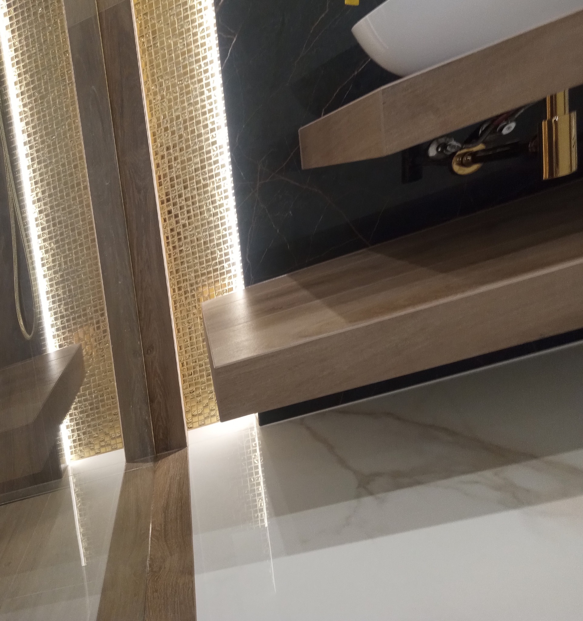 Nowoczesna łazienka z umywalką nablatową, drewnianym blatem i mozaiką w odcieniach złota, oświetlona listwą LED.