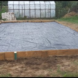 MAJO Piotr Kwiek - Przygotowany teren pod wylewkę fundamentów: szalunek z desek, folia i siatka zbrojeniowa. W tle szklarnia i cegły.