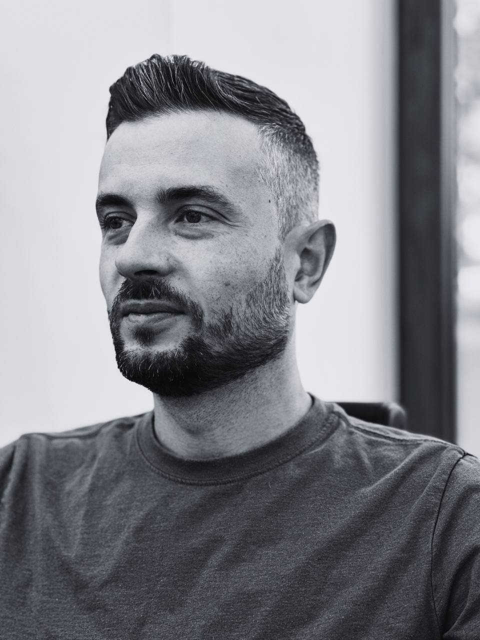 Portret mężczyzny z modną fryzurą typu pompadour i starannie przystrzyżoną brodą, czarno-białe zdjęcie z subtelnym oświetleniem bocznym.