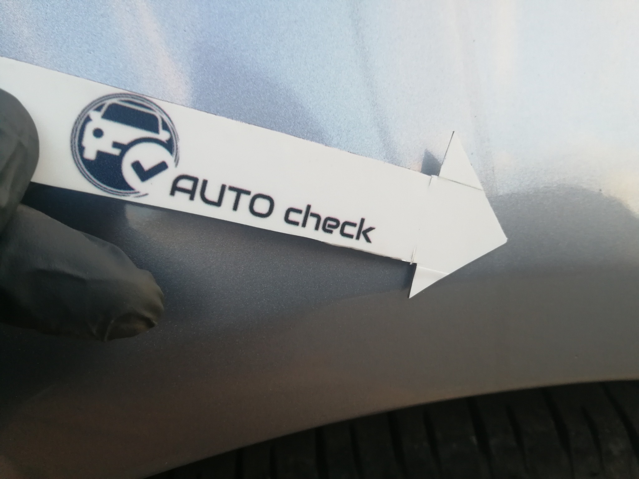 Pomiar grubości lakieru na srebrnym samochodzie za pomocą miernika 'AUTO check'.