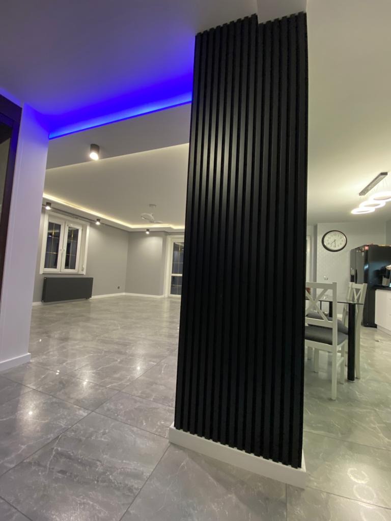 Nowoczesne wnętrze: szara marmurowa podłoga, czarna pionowa dekoracja ścienna z listew, sufit z niebieskim oświetleniem LED.