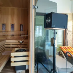 Ozonowanie sauny: urządzenie na statywie w saunie z drewna, widoczne ławy, kamienie i sprzęt do ozonowania.