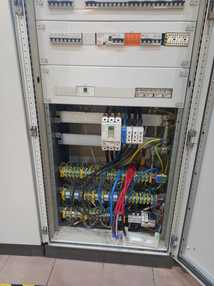 Otwarta szafa elektryczna z widocznymi bezpiecznikami, przewodami w kolorowych izolacjach i listwami zaciskowymi, wnętrze rozdzielnicy połączone z instalacją.