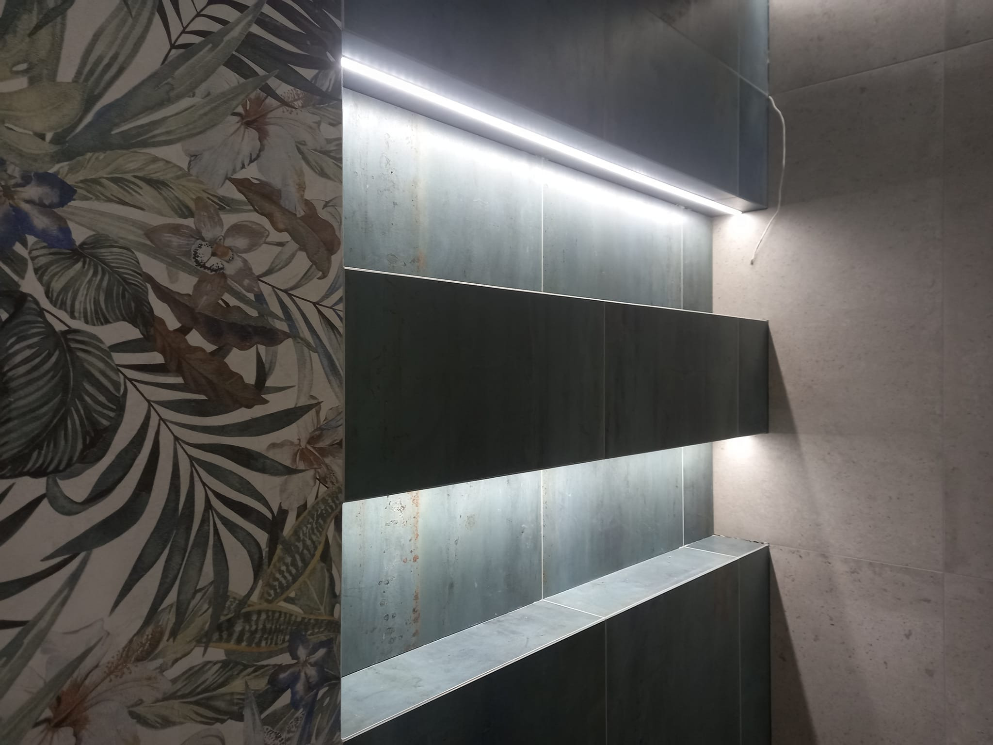 Półki ścienne w łazience z podświetleniem LED, jedna ściana z wzorem w liście i kwiaty, nowoczesny design.