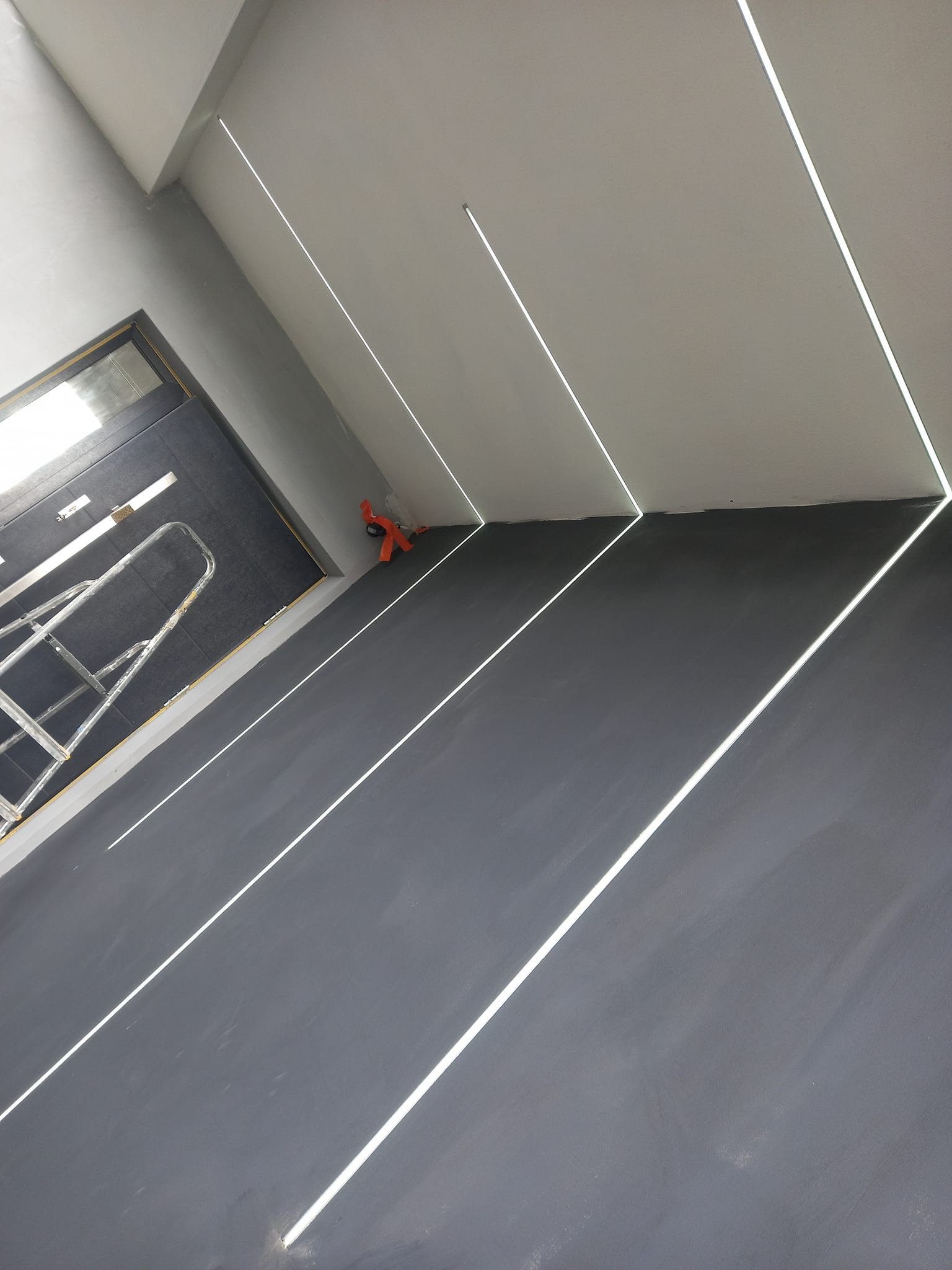 Montaż liniowego oświetlenia LED w suficie pod kątem, widoczna drabina i narzędzia montażowe.