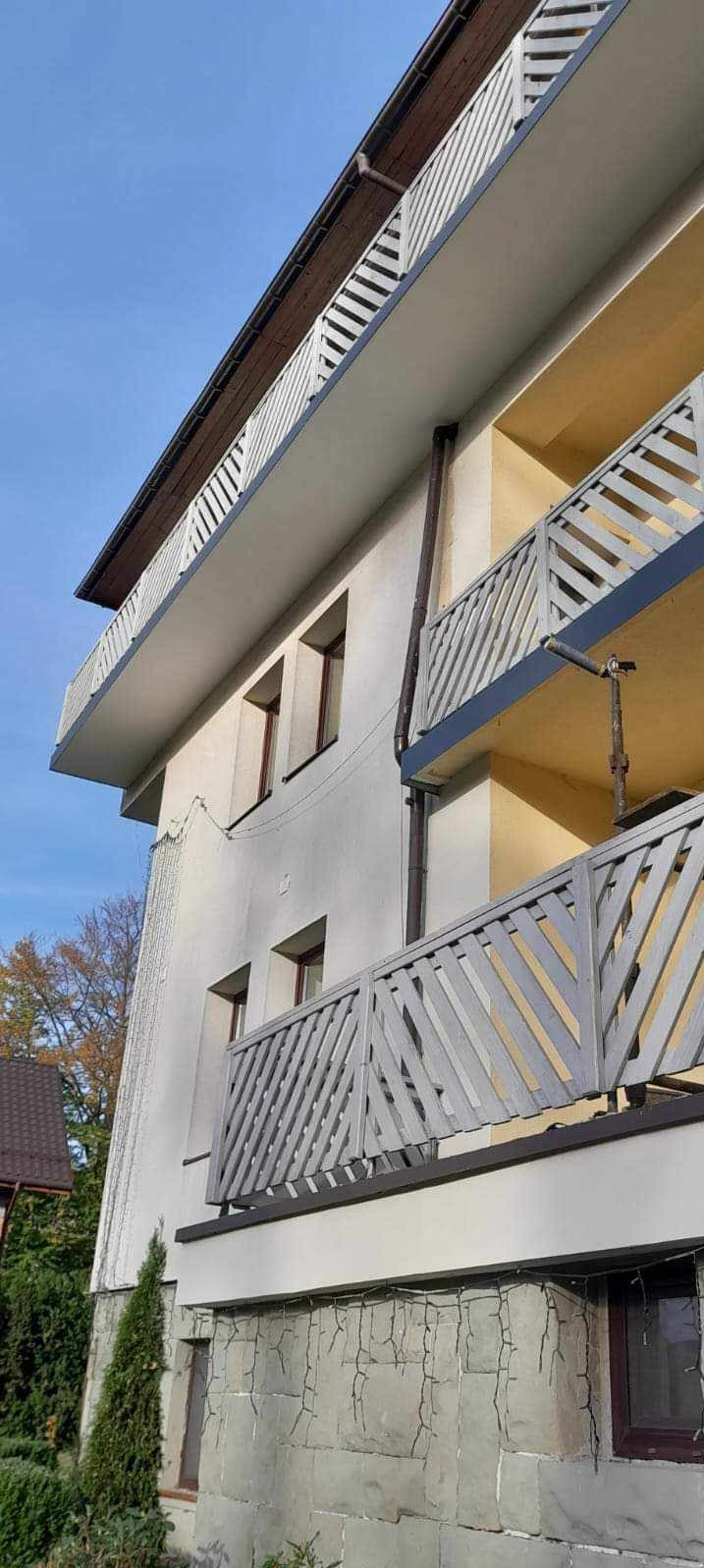 Wielopiętrowy budynek z balkonami po renowacji. Widoczne odnowione balustrady balkonowe o ukośnym wzorze, świeżo pomalowana elewacja oraz rynna spustowa. Na pierwszym planie fragment elewacji...