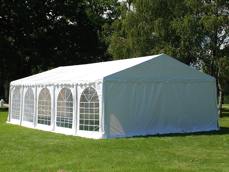 Rozłożony biały namiot imprezowy z oknami na trawniku, widok z zewnątrz, w tle drzewa.