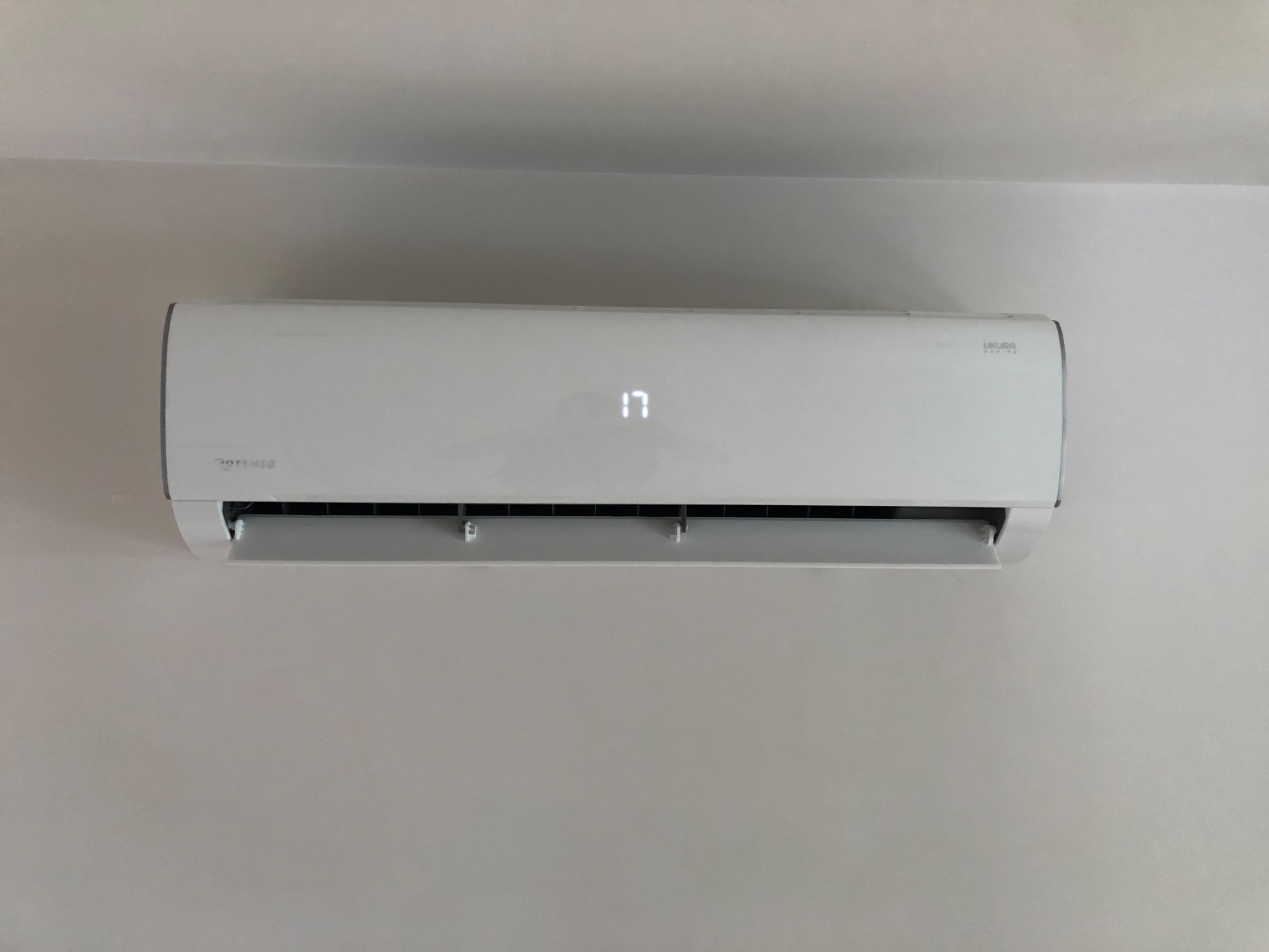 Biały klimatyzator ścienny z wyświetlaczem pokazującym temperaturę 17 stopni Celsjusza, zamontowany na jasnej ścianie.