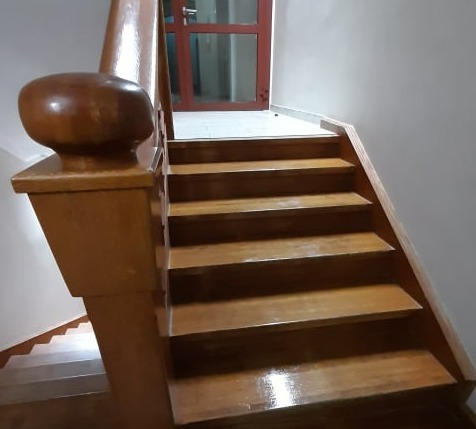 Drewniane schody w budynku biurowym, widok z dołu, poręcz z zaokrąglonym zakończeniem, drzwi z szybą w tle.