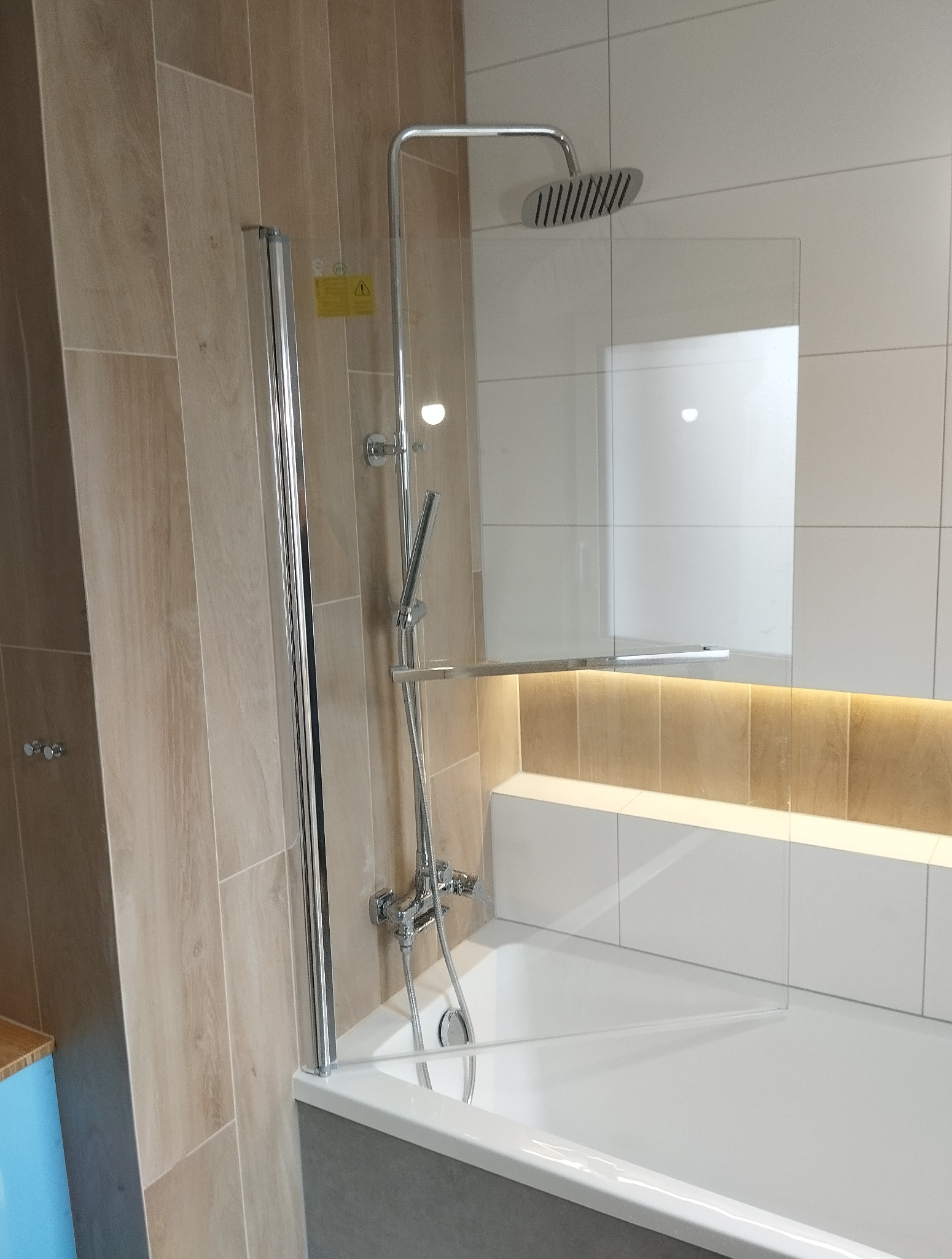 Nowoczesna kabina prysznicowa z transparentną szybą i chromowaną armaturą, wykończona beżowymi i białymi płytkami w łazience z subtelnym oświetleniem.