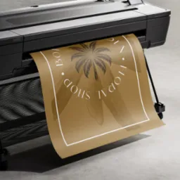 Szerokoformatowa drukarka atramentowa drukuje plakat w kolorze khaki z motywem palmy i napisem 'Boden Floral Shop' w okręgu.