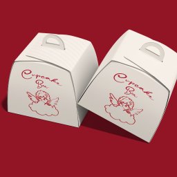 Nouva Atelier - Marta Lińska - Dwa białe pudełka na babeczki z uchwytem i rysunkiem aniołka na czerwonym tle. Opakowania z napisem 'Cupcake Box' w ozdobnej czcionce.