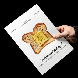Unfold Brand - Ręka w czarnym swetrze trzyma białą kartkę z grafiką tostowanej kromki chleba z masłem i pieprzem. Widoczne napisy 'independent bakery' i 'est. 2026'.