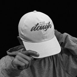 Unfold Brand - Czarno-białe zdjęcie osoby w szarej bluzie z kapturem, która naciąga białą czapkę z daszkiem. Na czapce widnieje czarny napis 'dough' oraz mniejszy tekst 'est. 2026 Bread Pastries Coffee'. Tło jest...