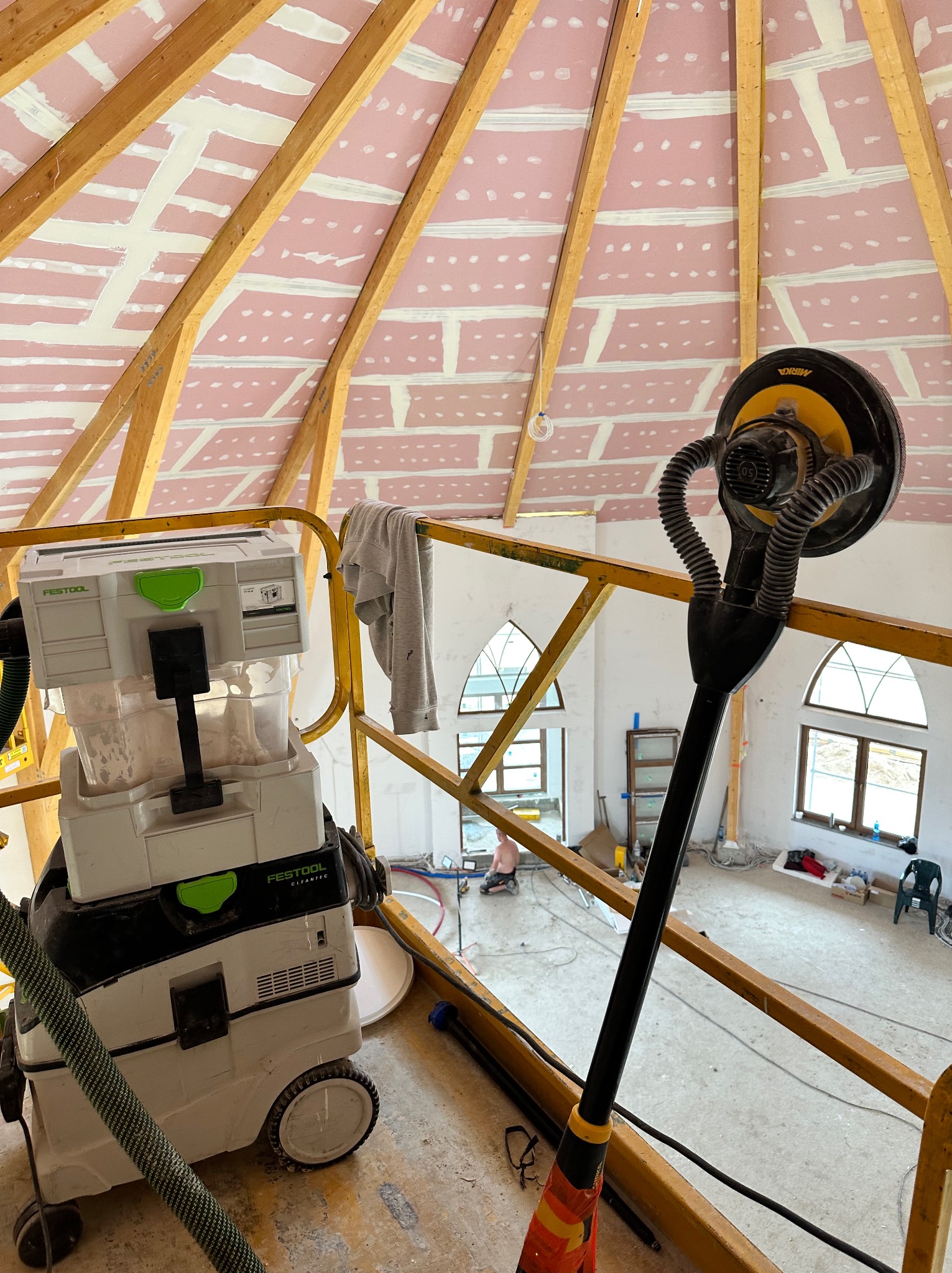 Sufit z płyt kartonowo-gipsowych na drewnianej konstrukcji, w trakcie szpachlowania łączeń, widoczny szlifierka do gipsu z odkurzaczem przemysłowym Festool, oraz fragment rusztowania.