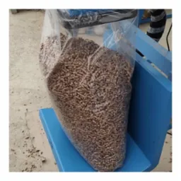 Worek z przezroczystego tworzywa wypełniony brązowym granulatem, ustawiony na niebieskiej platformie w pomieszczeniu o betonowej podłodze.