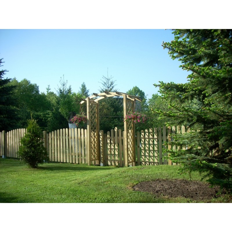 Świeżo postawione, jasne drewniane ogrodzenie panelowe z furtką zwieńczoną ażurową pergolą, na trawniku z młodymi drzewkami iglastymi, w tle zieleń drzew.