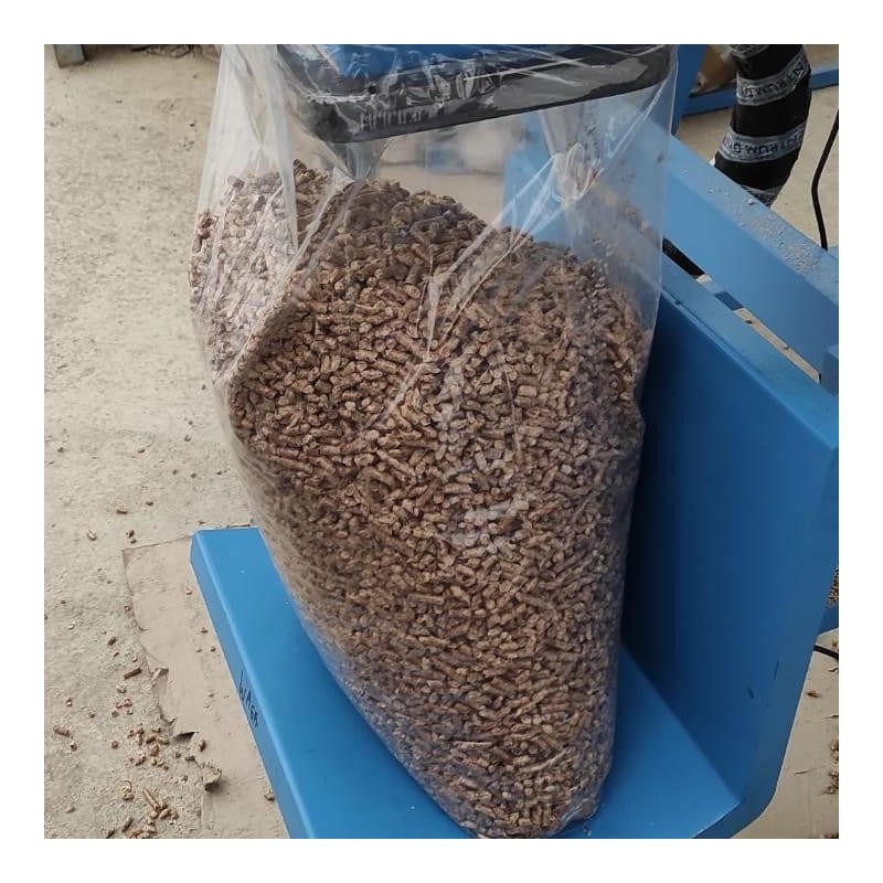 Worek wypełniony pelletem drzewnym, umieszczony na niebieskim, metalowym podłożu w hali produkcyjnej. Widoczne drobne ślady trocin na podłodze.