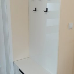 OPTIMEB Meble na wymiar Bartosz Figiel - Biała szafka z dwiema szufladami i panelem z wieszakami w przedpokoju, czarne uchwyty i wieszaki, minimalistyczny design.