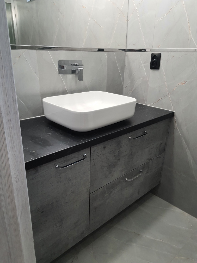 Nowoczesna łazienka z umywalką nablatową o kwadratowym kształcie, szarą szafką z dwiema szufladami o fakturze betonu i marmurową okładziną ścienną w odcieniach szarości.