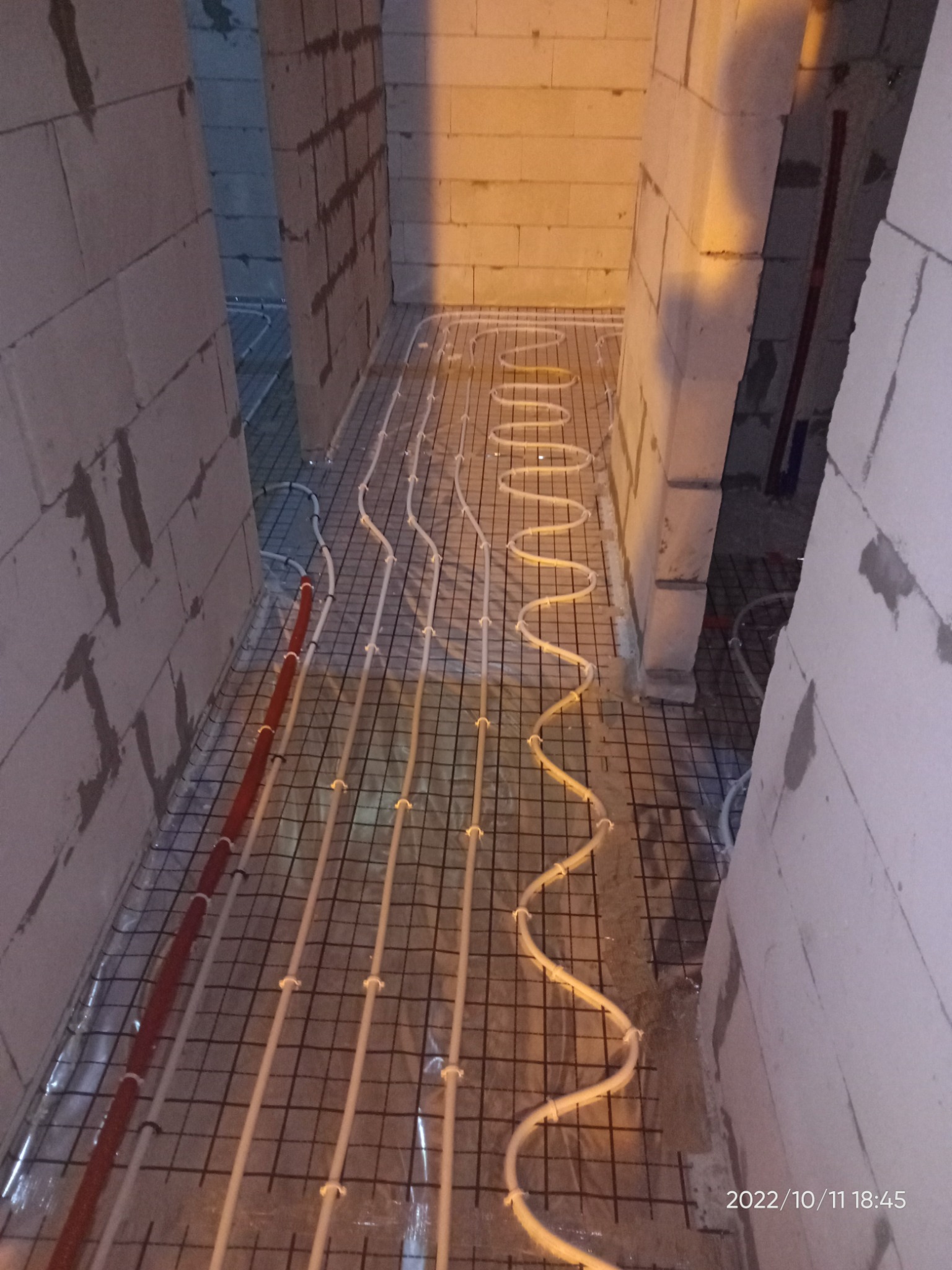 Rozłożone rury ogrzewania podłogowego na siatce w trakcie instalacji w Suwałkach, widoczne fragmenty ścian z bloczków betonowych.