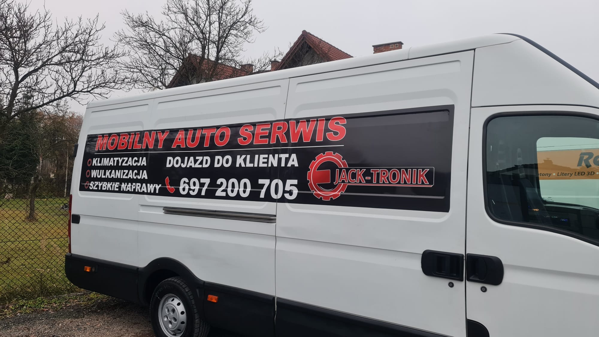 Biały samochód dostawczy z czarną grafiką reklamową mobilnego serwisu samochodowego z informacjami o klimatyzacji, wulkanizacji, dojeździe do klienta i numerem telefonu.