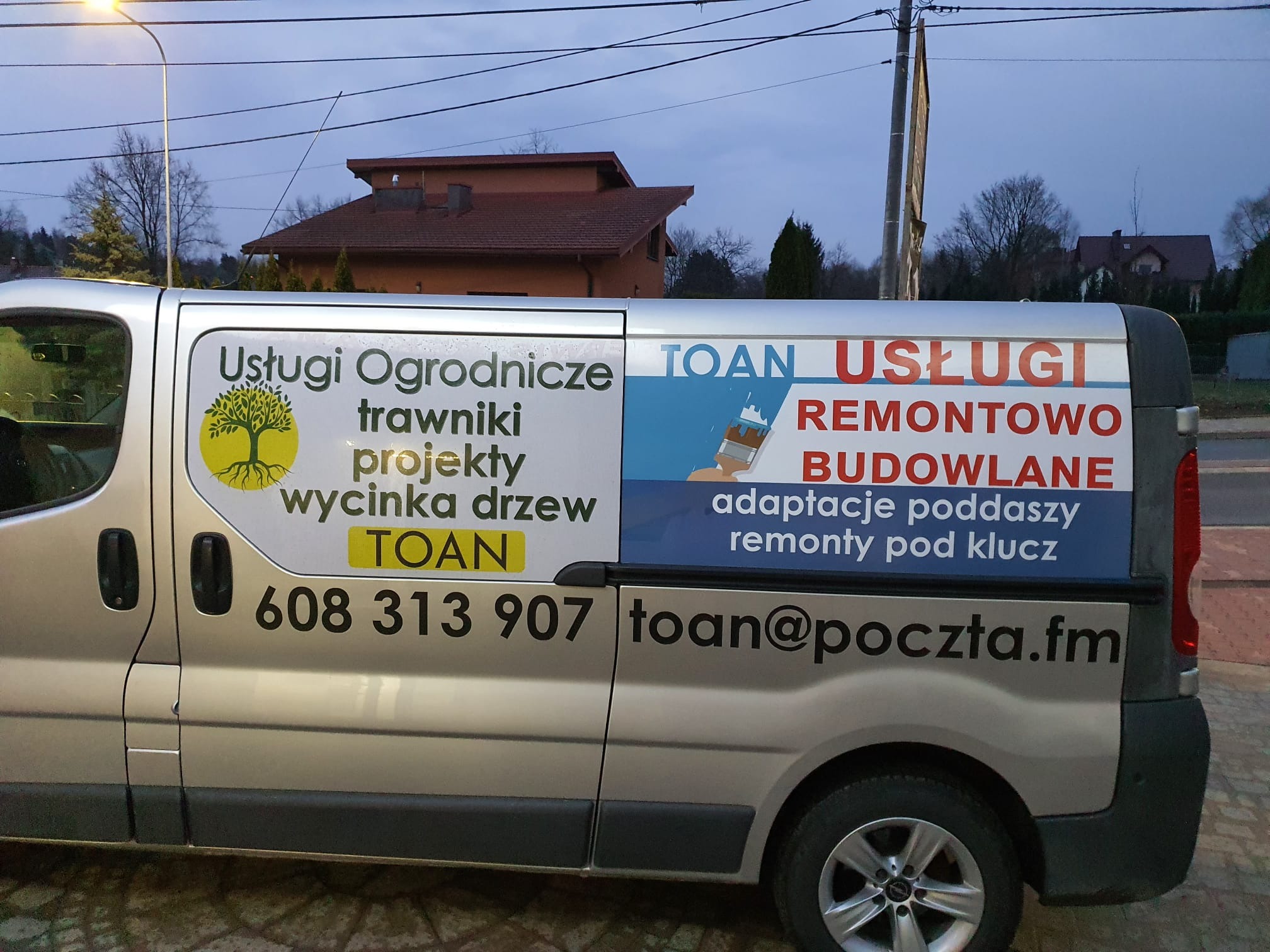 Srebrny samochód dostawczy z reklamą usług ogrodniczych, remontowych i budowlanych firmy TOAN, z numerem telefonu i adresem e-mail.