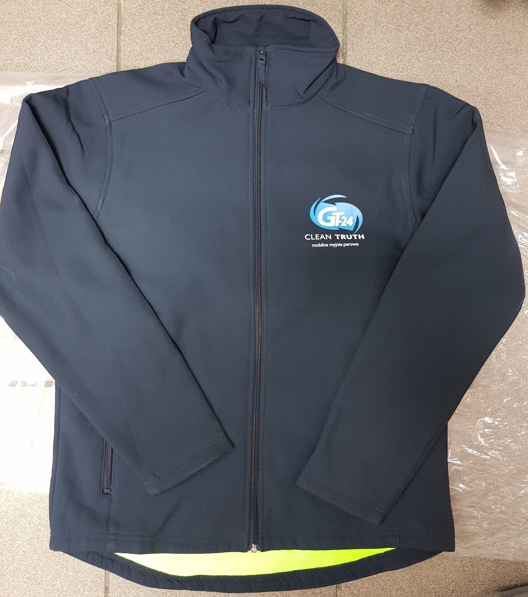 Granatowa kurtka softshell z zamkiem błyskawicznym, logo 'GT24 CLEAN TRUTH mobilna myjnia parowa' na lewej piersi i jaskrawożółtym wykończeniem u dołu.